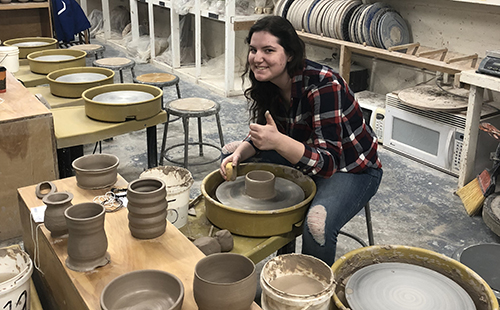 Junior Sam McCoy, who is interested in minoring in art, poses while in the progress of throwing on the potter's wheel at the University of Kansas on March 2.