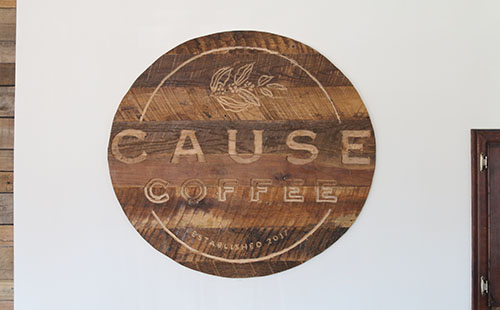 A handmade wooden sign displaying the shop’s logo adorns the front wall of Cause Coffee.