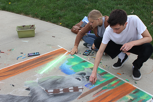 Seniors Sam McGuire and Carly Bodenhausen work on the background of a sidewalk chalk drawing for the Frontier League art show. The theme was to turn the school's mascot into a Jedi Knight.