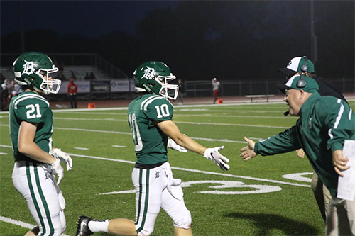 Sophomore Tyson Priddy (left) and senior Keegan Sturdy (right) run to high-five coach Brian King at the game against Wyandotte High School on Sept. 7.