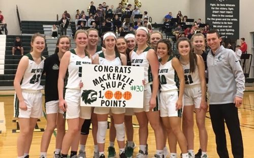 The De Soto High School varsity girls’ basketball team poses with senior Mackenzie Shupe to congratulate her on reaching one thousand total career points after the game against Turner High School on Feb. 11. 